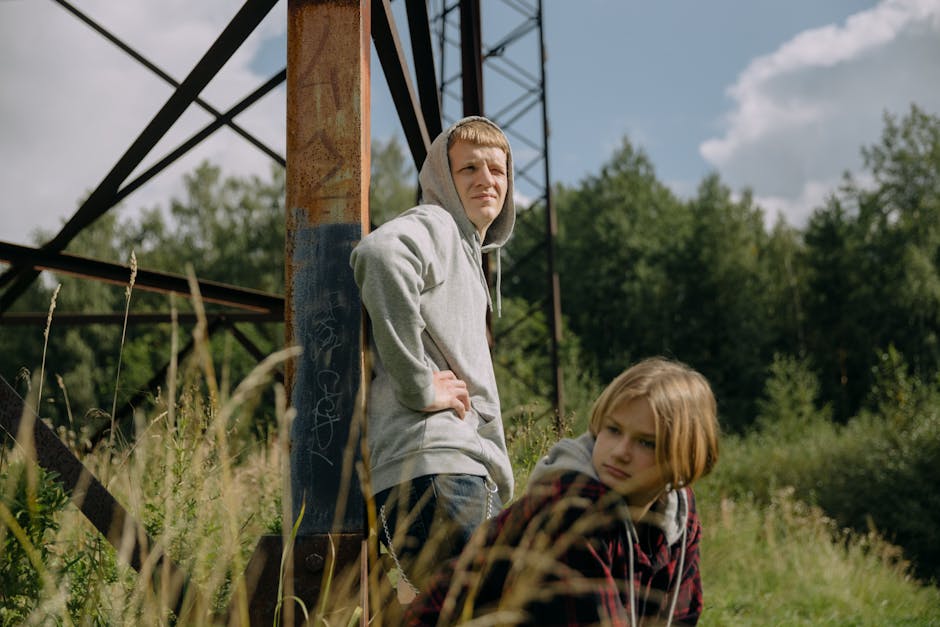 Two young siblings outdoors near electricity pylon surrounded by greenery.