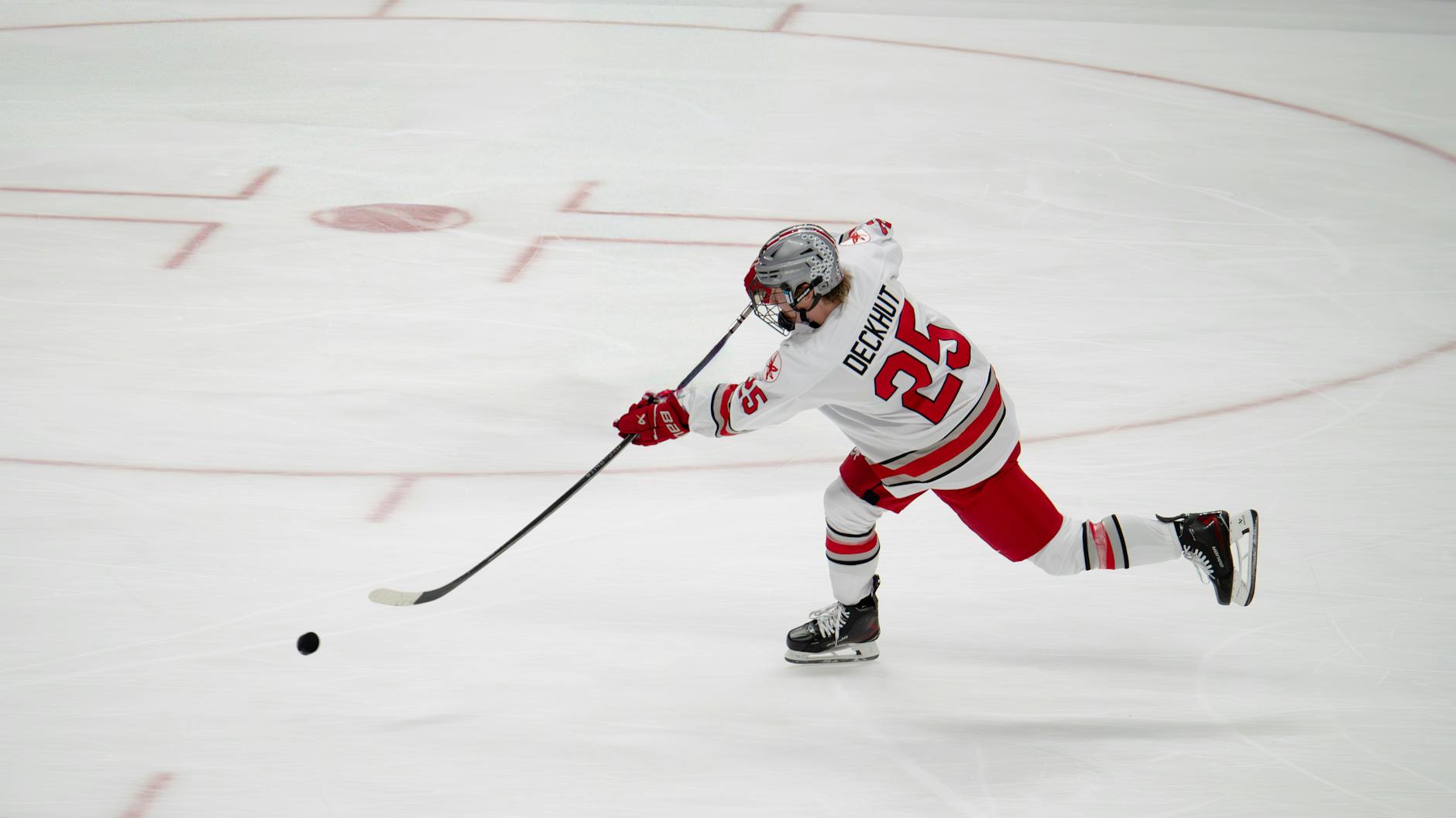 A professional ice hockey player takes a powerful shot on a rink.